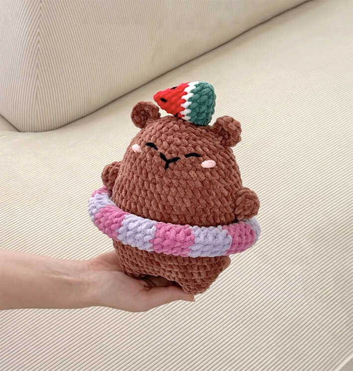 Capybara amigurumi free crochet pattern featuring a plush handmade toy with a watermelon hat and colorful swim ring, held in hand
