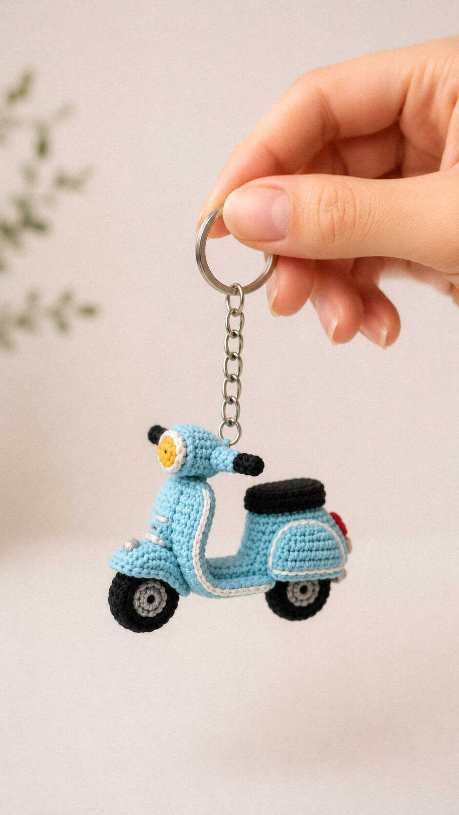 Tiny crochet Vespa keychain in light blue yarn held by hand against a soft neutral background